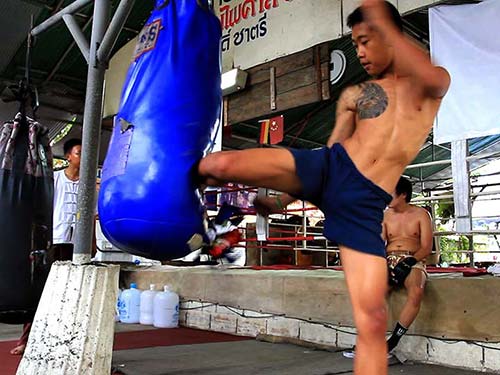 Boxer training in a gym, kicking a sack.